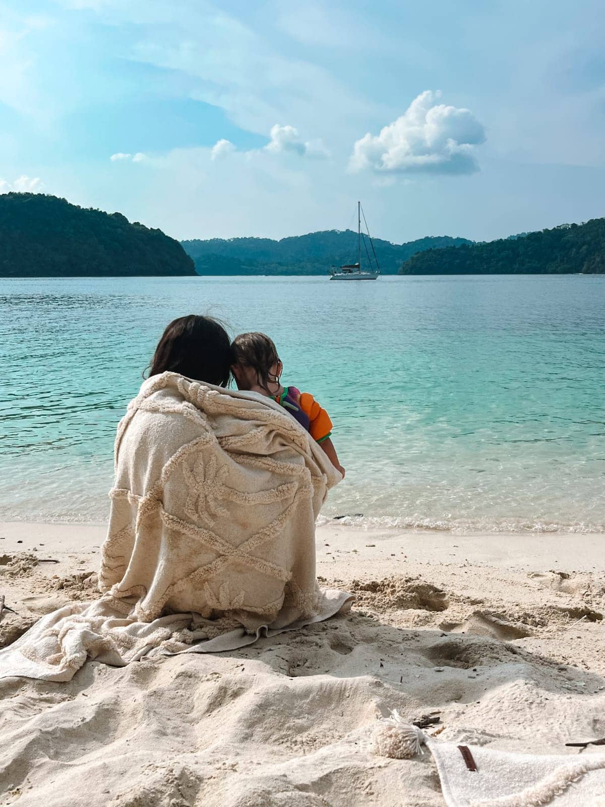 Two people sitting on a sandy beach with a boat in the distance.